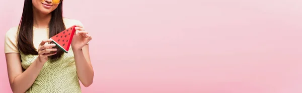Cultivo panorámico de niña positiva sosteniendo en rodajas de papel sandía aislado en rosa - foto de stock