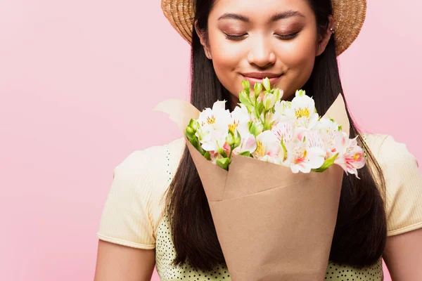 Positive asiatique fille en paille chapeau odeur fleurs isolé sur rose — Photo de stock