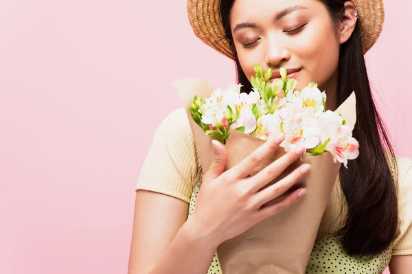 Young asian woman in straw hat smelling flowers isolated on pink — Stock Photo