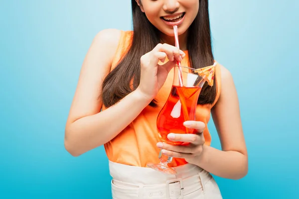 Обрезанный вид счастливой девушки, держащей стакан с коктейлем на голубом — стоковое фото