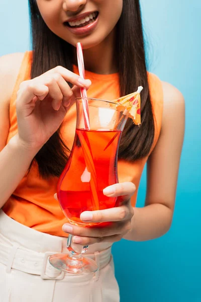 Cropped view of cheerful girl holding glass with cocktail on blue — Stock Photo