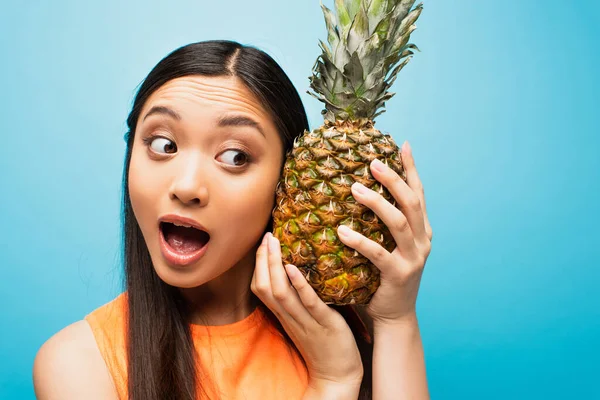 Excited asian girl holding ripe pineapple on blue — Stock Photo