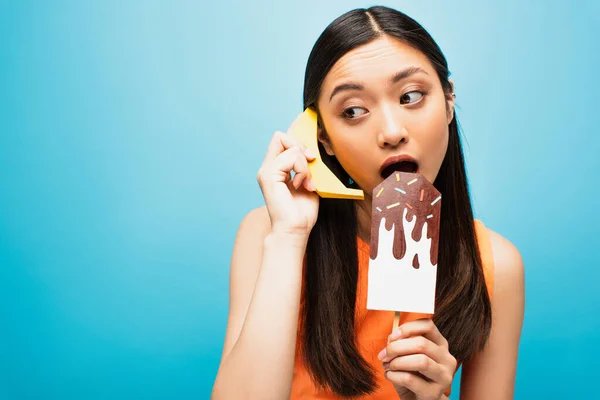 Asiático chica con abierto boca celebración plátano y papel hielo grito en azul - foto de stock