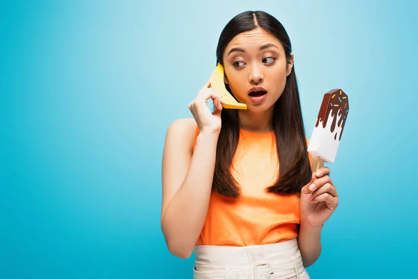 Beautiful asian girl holding banana and paper ice scream on blue — Stock Photo