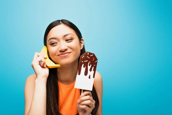Happy asian woman holding fresh banana and paper ice scream on blue — Stock Photo
