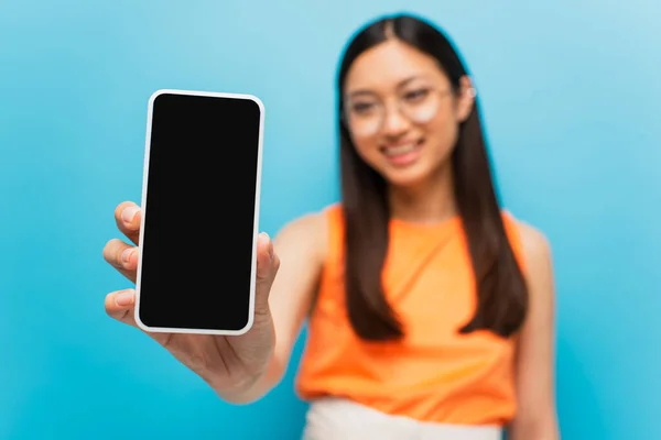 Foco seletivo de menina asiática feliz segurando smartphone com tela em branco isolado no azul — Fotografia de Stock