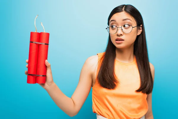 Emotional asian girl in glasses holding dynamite sticks on blue — Stock Photo