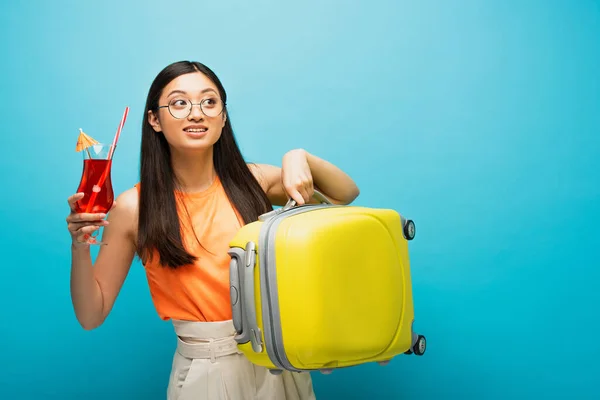 Счастливая девушка в очках, держащая в руках коктейль и мешок, отводя взгляд в сторону от синего — стоковое фото