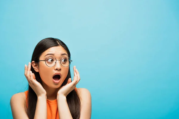 Überrascht asiatische Frau mit Brille gestikuliert und sieht weg auf blau — Stockfoto