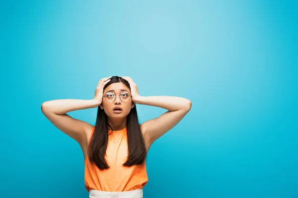 Sorpreso asiatico donna in occhiali toccare testa su blu — Foto stock