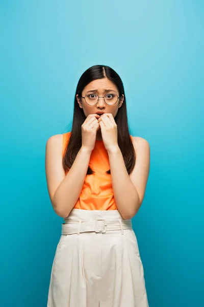 Young and scared asian woman touching mouth on blue — Stock Photo