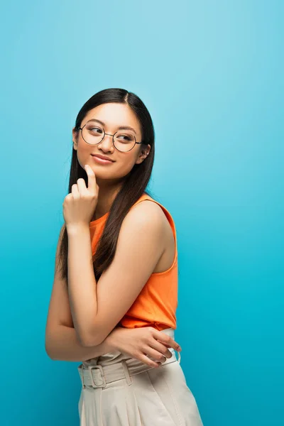 Gai asiatique fille dans lunettes sourire et regarder loin isolé sur bleu — Photo de stock