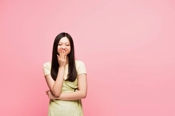 Happy asian girl covering mouth isolated on pink — Stock Photo