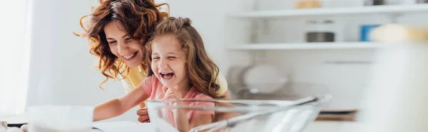 Selective focus of excited mother and daughter laughing while cooking in kitchen, website header — Stock Photo