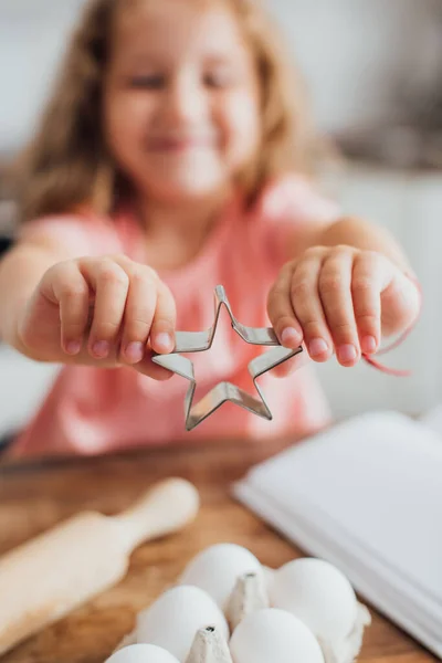 Selective focus of kid showing star-shaped cookie cutter near chicken eggs — Stock Photo