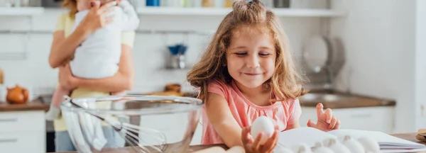 Fuoco selettivo di figlia che tiene uovo di pollo vicino a madre con figlio neonato, colpo panoramico — Foto stock