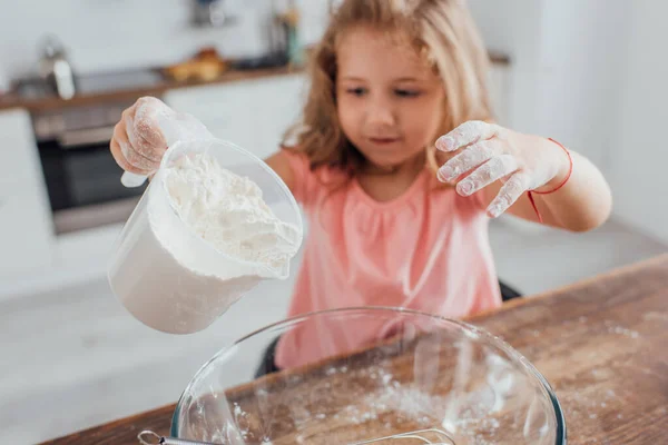 Foco seletivo da menina loira derramando farinha em tigela de vidro enquanto cozinha na cozinha — Fotografia de Stock