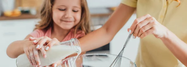 Ausgeschnittene Ansicht der Mutter mit Schneebesen, die zusammen mit ihrer Tochter Milch in eine Glasschüssel gießt, Panoramaaufnahme — Stockfoto
