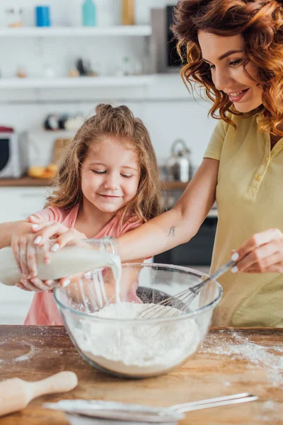 Foco seletivo da menina com a mãe derramando leite em tigela de vidro com farinha — Fotografia de Stock