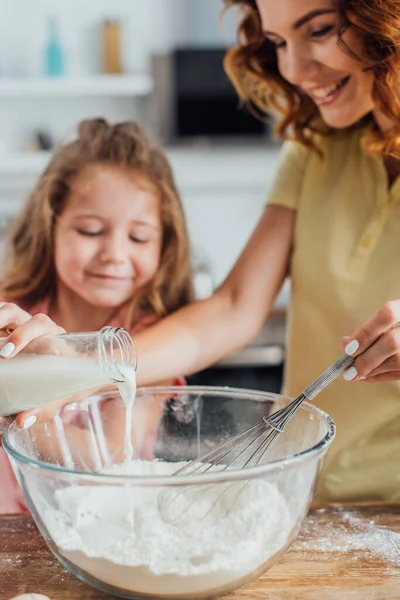 Foco seletivo da mulher derramando leite em tigela com farinha perto da filha — Fotografia de Stock