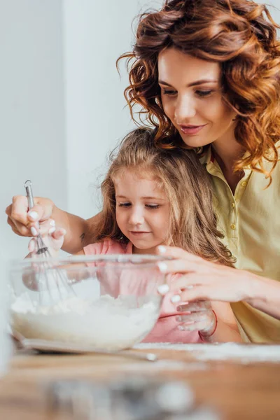 Enfoque selectivo de la madre joven amasando masa en un tazón de vidrio cerca de la hija — Stock Photo