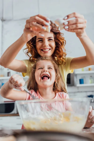 Selective focus of mother adding egg into glass bowl while excited daughter kneading dough — Stock Photo