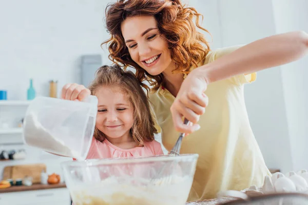 Messa a fuoco selettiva di mamma impastare pasta in ciotola di vetro vicino figlia — Foto stock