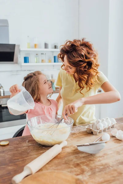 Selective focus of mother kneading dough while looking at daughter in kitchen — Stock Photo