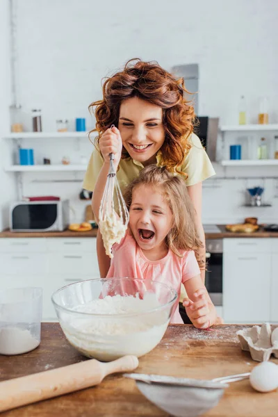 Foyer sélectif de fille excitée tenant fouet avec pâte près de la mère — Photo de stock