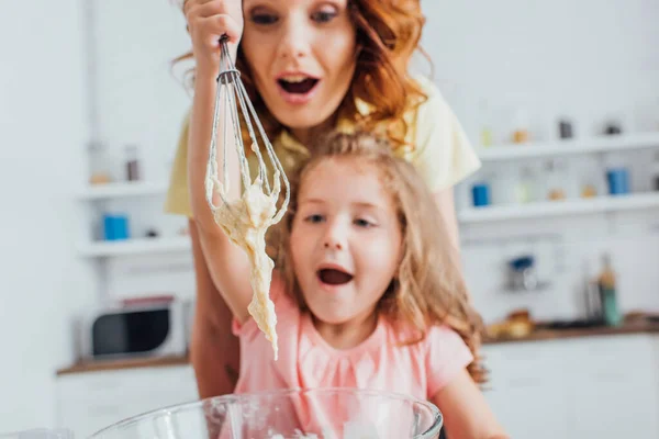 Messa a fuoco selettiva di madre e figlia eccitate guardando la pasta sulla frusta durante la cottura in cucina — Foto stock