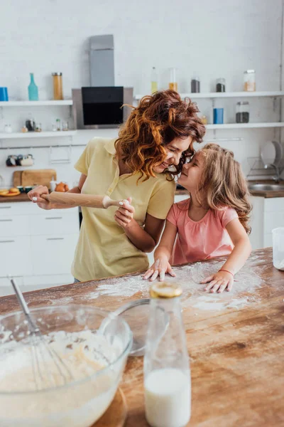 Selektiver Fokus von Mutter mit Nudelholz und Tochter, die Mehl verstreut, während sie direkt am Küchentisch steht — Stockfoto