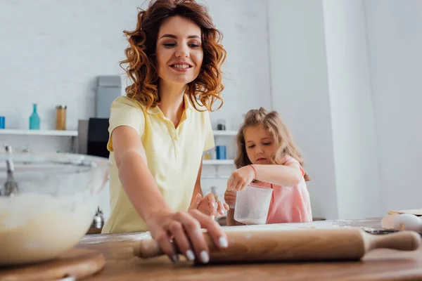 Selektiver Fokus der Mutter mit Nudelholz in der Nähe der Tochter, die Maßkrug hält — Stockfoto