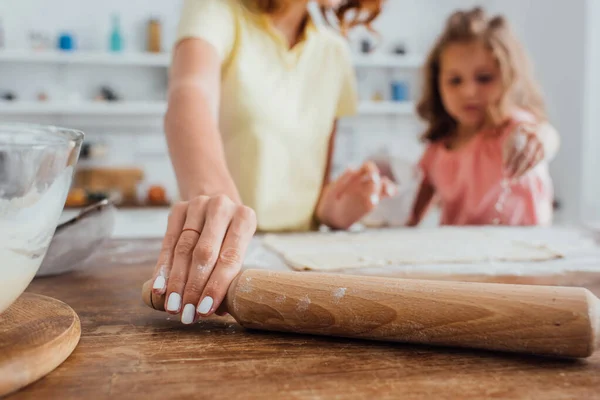 Abgeschnittene Ansicht der Mutter, die Nudelholz in der Nähe der Tochter und Teig auf dem Küchentisch nimmt, selektiver Fokus — Stockfoto