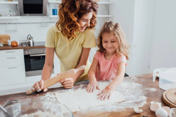 Foyer sélectif de fille touchant la pâte roulée près de la mère tenant rouleau à pâtisserie — Photo de stock