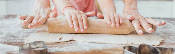 Partial view of woman and child rolling out dough near cookie cutters on kitchen table, panoramic shot — Stock Photo