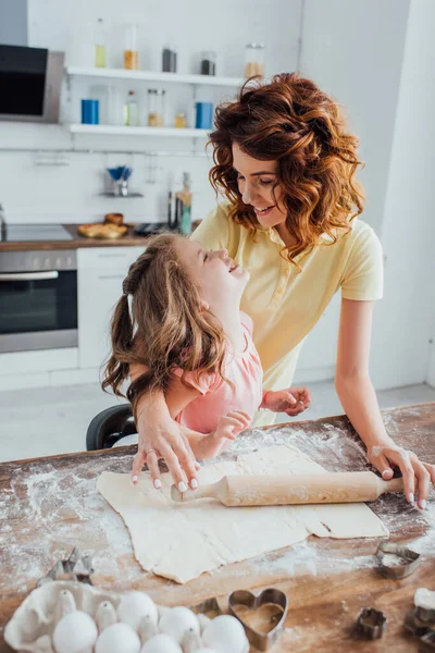 Selective focus of mother and daughter looking at each near rolled dough, chicken eggs and cookie cutters on kitchen table — Stock Photo