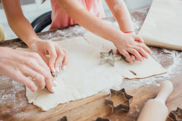 Vista parcial de la mujer y el niño cortando galletas de masa laminada cerca de moldes en forma de estrella — Stock Photo