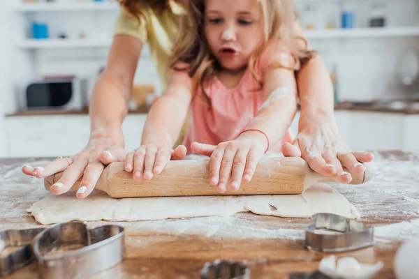 Vista recortada de la hija con nom despliegue de masa cerca de cortadores de galletas, enfoque selectivo — Stock Photo