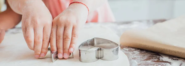 Partial view of kid cutting out cookies from rolled dough with molds — Stock Photo