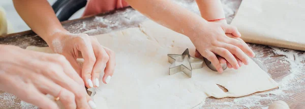 Visión parcial de la mujer y el niño cortando las galletas de la masa laminada cerca del molde en forma de estrella, concepto panorámico - foto de stock
