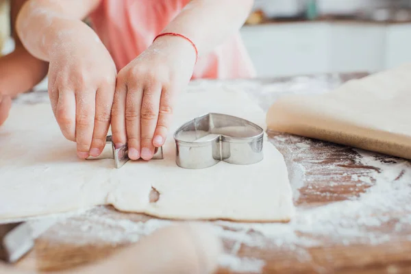 Ausgeschnittene Ansicht eines Kindes, das Kochen aus ausgerolltem Teig auf einem mit Mehl bestreuten Tisch ausschneidet — Stockfoto