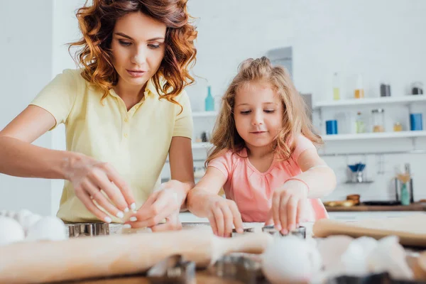 Selektiver Fokus der lockigen Mutter und der blonden Tochter beim gemeinsamen Zubereiten von Plätzchen in der Küche — Stockfoto