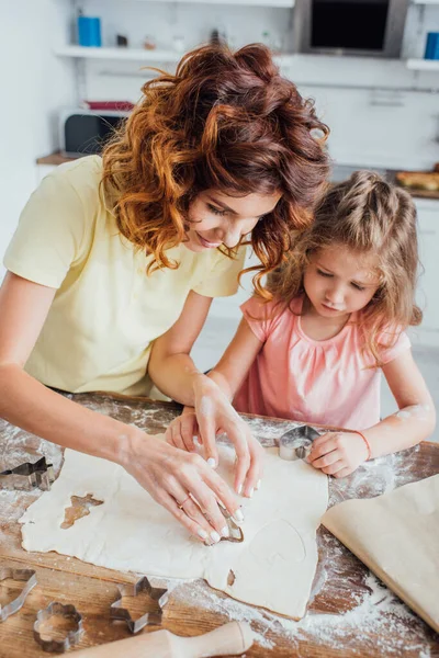 High angle view of curly mom and blonde daughter cutting out cookies from rolled dough — Stock Photo
