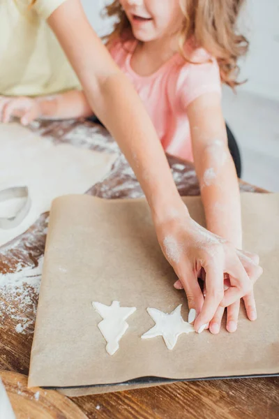 Teilansicht einer Frau mit Tochter, die rohe, mehrförmige Plätzchen auf Backpapier legt, selektiver Fokus — Stockfoto