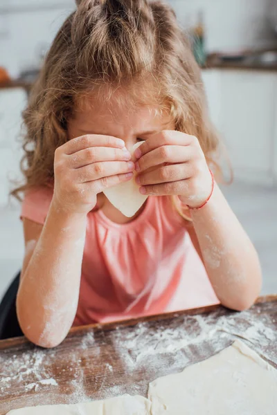 Petite fille tenant morceau de pâte en forme de coeur tout en préparant des biscuits dans la cuisine — Photo de stock