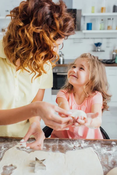 Selective focus of mother holding raw cookie near daughter, rolled dough and star-shaped mold — Stock Photo