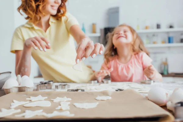 Selective focus of raw multi-shaped cookies on baking paper near mother and daughter — Stock Photo