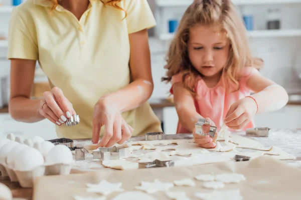 Cropped view of mother and daughter cutting out cookies near chicken eggs on kitchen table, selective focus — Stock Photo