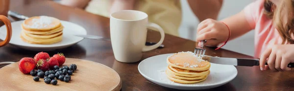 Vue recadrée de fille prenant le petit déjeuner tout en mangeant de délicieuses crêpes, image horizontale — Photo de stock