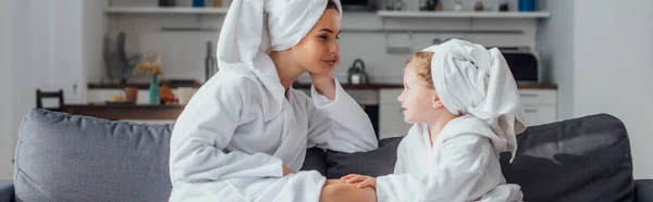 Daughter and mother talking while sitting on sofa in bathrobes and towels on heads, panoramic shot — Stock Photo